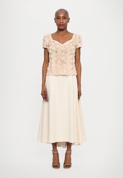 Rosa blomstret topp med puff-sleeves, kombinert med en lang elfenbensfarget skjørt og beige sandaler med stropper, som skaper et lagdelt, elegant antrekk.