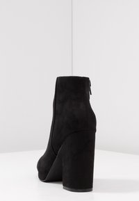 Sort ruskindsankelstøvle med høj blokhæl og lynlås i siden. Designet har en glat tekstur og en afrundet tå.