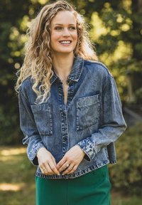 Denimjack met een relaxte pasvorm, lichtblauwe wassing, puntige kraag, twee borstzakken en contrasterende stiksels, gecombineerd met groene broek.