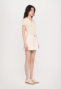 Světle béžové polo tričko s krátkým rukávem, spárované s krémovou plisovanou mini sukní a krémovými teniskami s barevnými pruhy. Minimalistický design.