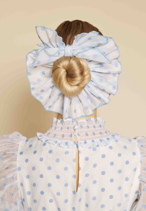 Blondt hår stylet i en stram knold pyntet med en stor gennemsigtig hvid sløjfe med blå polkaprikker, som matcher den flæsekantede kjole.