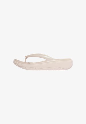 Beige gevoerde teenslipper met een dikke zool en gebogen teenriem, ontworpen voor casual gebruik en comfort.
