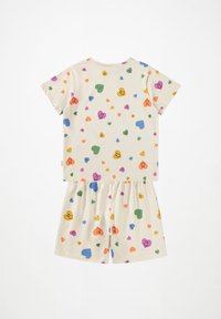 Completo pigiama in cotone crema con maniche corte e pantaloni corti. Presenta motivi colorati di cuori e faccine sorridenti. Vita elastica sui pantaloni.
