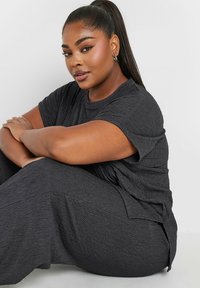 Musta tekstuuriga vabaaja komplekt, mis sisaldab lühikeste varrukatega toppi ja laia jalaga pükse, loodud mugavuseks ja lõõgastumiseks.