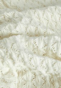 Manta de punto en crema con un patrón texturizado y de encaje que presenta motivos en zigzag y hojas, mostrando fibras suaves y una sensación ligera.