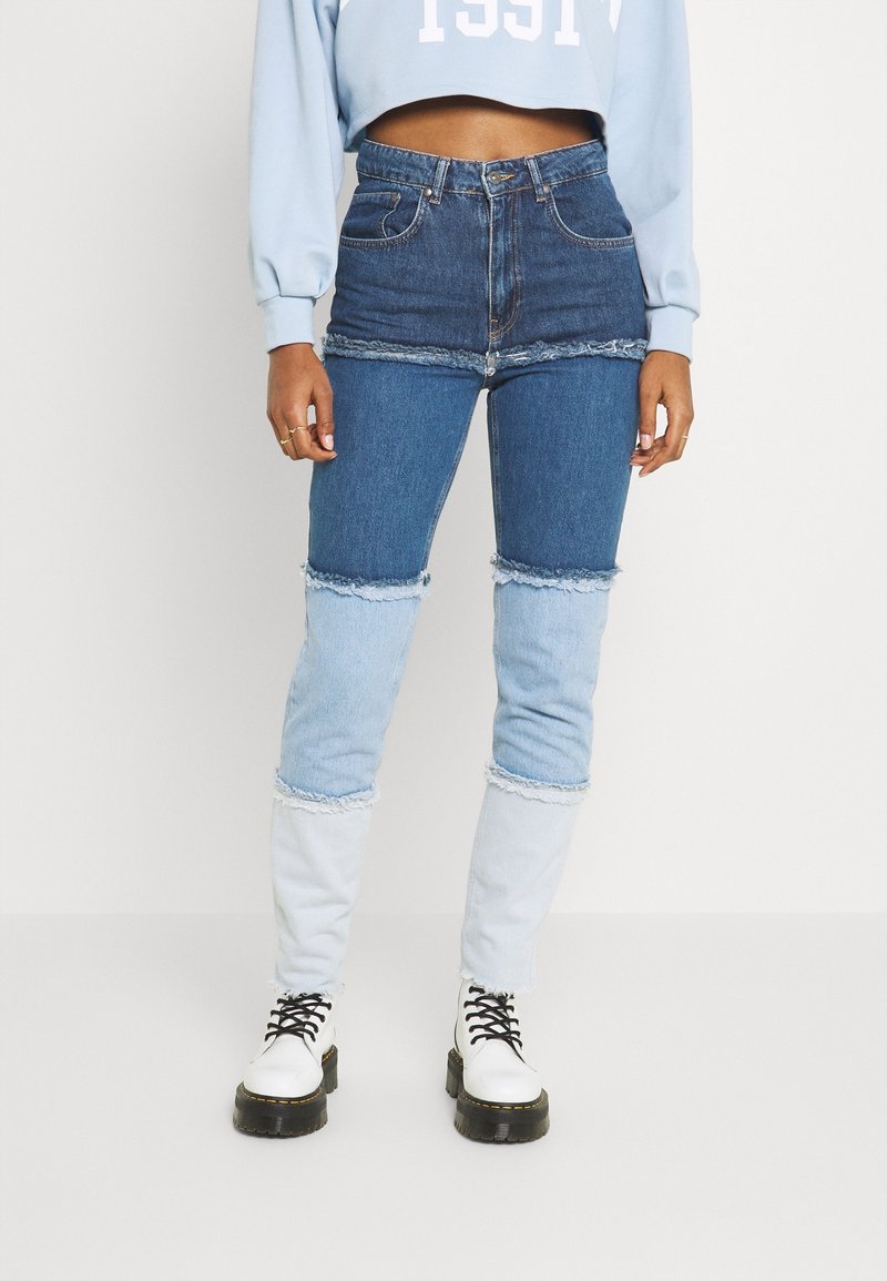 Jeans de mezclilla con un diseño de patchwork que combina tonos de azul oscuro y claro. Presentan bordes deshilachados y un corte de cintura alta. Combinados con botas blancas.