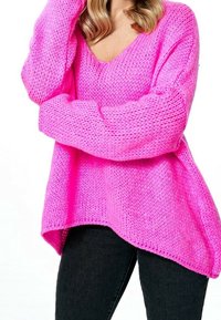 Svetle růžový, volný pletený svetr s hlubokým výstřihem do V a dlouhými rukávy, s zakřiveným lemem a texturovanou tkaninou. Spárováno s černými džíny.