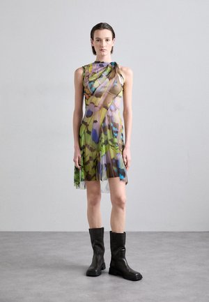 Mehrfarbiges Kleid mit einem transparenten Überzug, das ein Blumenmuster in Grün, Blau und Braun zeigt. Kombiniert mit schwarzen Stiefeln bis zum Knie.