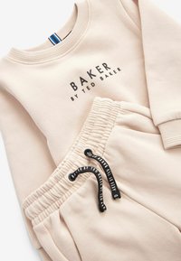Beige sweatshirt og matchende joggers med "BAKER BY TED BAKER" trykt på forsiden, med en snor i taljen og blød tekstur.