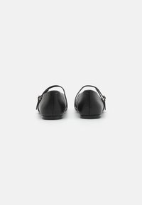 Sorte skinnflats med ankelrem, avrundet tå og en liten gullakcent. Jevn tekstur og minimalistisk design. Bakfra vises.