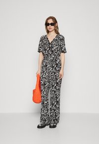 Combinaison à motifs floraux noir et blanc avec des manches courtes et une taille cintrée. Assortie à un sac orange et des chaussures noires imposantes.