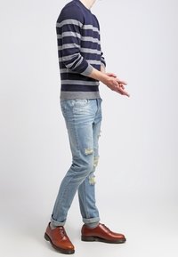 Maglione a righe blu navy e grigio, jeans strappati azzurri chiari e scarpe eleganti marroni. Il maglione ha un collo rotondo e polsini a costine.