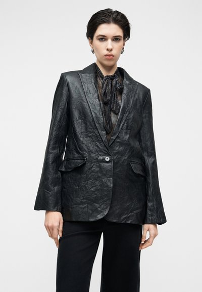 Μαύρο δερμάτινο σακάκι με υφή φινιρίσματος, κλείσιμο με ένα κουμπί και πέτο με χαραγμένη εγκοπή. Διαθέτει δύο μπροστινές τσέπες και μακριά μανίκια.