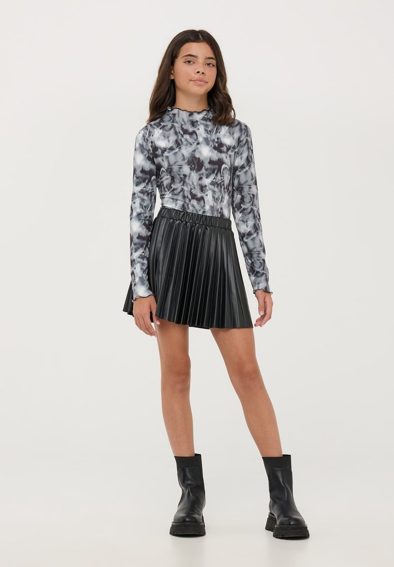 Maglietta a maniche lunghe in un motivo marmorizzato bianco e nero, abbinata a una gonna nera plissettata. La modella indossa stivali neri alla caviglia. Tessuto dalla superficie liscia.
