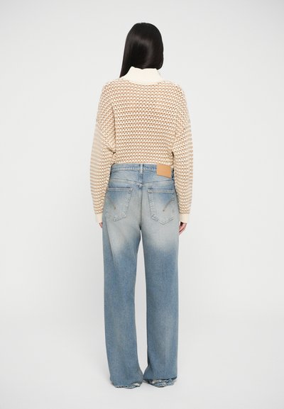 Beige knit sweater with a high collar, paired with light blue slightly distressed wide-leg jeans featuring a brown leather patch at the back.
