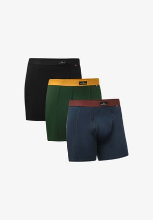 Tres pares de calzoncillos de estilo boxer en negro, verde con una cinturilla amarilla y azul marino con una cinturilla marrón. Fabricados de algodón, con un diseño típico de canesú.