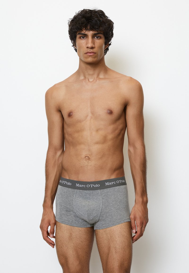Boxer in cotone grigio con una texture morbida e un cinturino nero a contrasto che mostra la scritta "Marc O'Polo" in lettere bianche. Il modello posa su uno sfondo neutro.