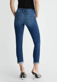 Jeans ajustados de color azul oscuro con puños enrollados y dos bolsillos traseros. Sutil detalle de costura en los bolsillos. Textura de denim suave.
