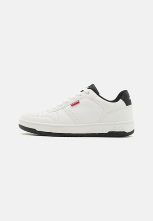 Hvid sneaker med lavt snit, sort sål og hæl, perforeret tå, hvide snørebånd og lille rød Levi's logo-tag på siden.