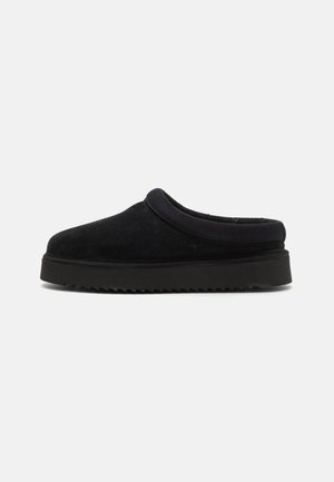 Black suede slip-on shoe with a rounded toe, featuring a cushioned upper and a ridged rubber sole. Smooth texture, minimal design.