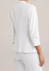 Valkoinen bleiseri, jossa on kolme neljänneksen hihaa, sileä pinta, ei näkyviä sulkijoita ja räätälöity siluetti, yksinkertainen muotoilu.