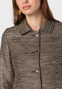 Brončani tweed sako s ovratnikom, koji ima četiri metalna gumba i teksturiranu tkaninu s suptilnim sjajnim detaljima.