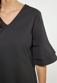 Zwarte top met een V-hals en korte mouwen, voorzien van gelaagde ruches. Het materiaal heeft een soepele textuur, geschikt voor casual kleding.