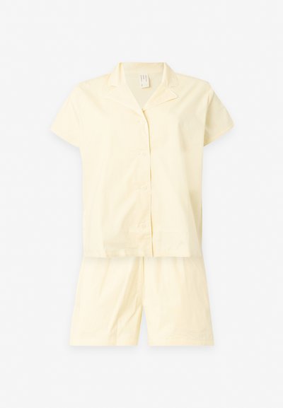 Haut de pyjama crème à manches courtes et boutonné, assorti à un short crème assorti sur fond blanc.