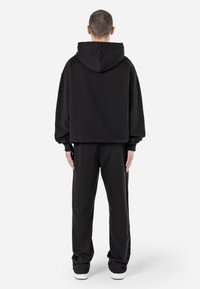 Svart oversized hoodie med huva, med långa ärmar och avslappnad passform, i kombination med matchande svarta sweatpants och vita sneakers.