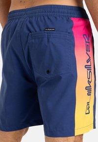 Shorts de baie pentru bărbați în albastru marin cu un panou lateral în degradé de la roz la galben. Dispune de un elastic în talie și un buzunar la spate cu închidere prin apăsare.