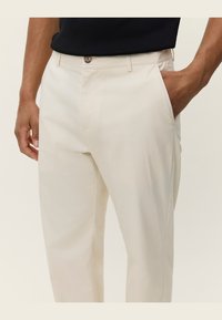 Pantaloni bej dintr-un material neted, cu picioare drepte, închidere cu nasture și buzunare laterale, având un luciu subtil și fără modele vizibile.