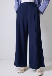 Pantalones de pierna ancha en color navy con cintura elástica, que cuentan con bolsillos laterales y una textura de tela suave. Combinados con zapatillas blancas.