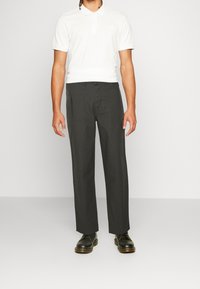 Grau Hosen mit geradem Schnitt, ausgestattet mit Seitentaschen und einem strukturierten Stoff. Kombiniert mit einem schmal geschnittenen weißen Poloshirt und schwarzen Schuhen.