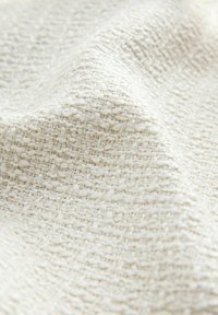 Gros plan d’un tissu crème texturé avec un motif tissé et des fibres légèrement surélevées créant une surface douce et irrégulière.