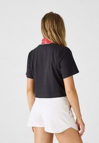 Camiseta negra recortada de algodón suave con mangas cortas, combinada con pantalones cortos gris claro. Bufanda roja visible alrededor del cuello.
