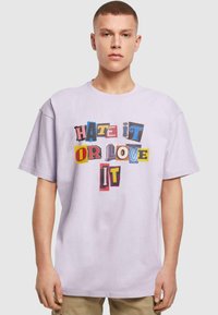 Lyse lilla oversized t-shirt med et flerfarvet grafisk tekstdesign, der står "HATE IT OR LOVE IT" i forskellige stilarter og farver.