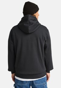 Felpa nera con cappuccio realizzata in tessuto morbido, caratterizzata da una vestibilità comoda, un cappuccio ampio e polsini a costine. Abbinata a jeans di denim.