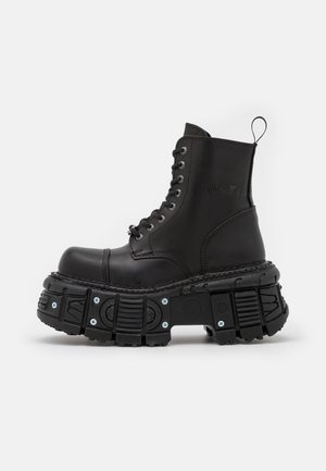Bottes de combat en cuir noir avec une tige haute, fermeture à lacets, semelle en caoutchouc épaisse et accents métalliques à la base de la semelle.