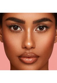 Gros plan sur un visage avec une peau lisse et éclatante, des yeux brun foncé, des lèvres pleines avec une finition brillante, et des sourcils bien définis, le tout sur un fond rose.