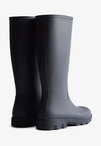 Bottes en caoutchouc noires étanches avec un design haut, des accents texturés sur le dessus et une semelle robuste pour une meilleure adhérence.