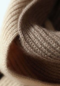 Tessuto a maglia beige a coste, con una texture morbida, arrotolato ai bordi, che mette in risalto fibre sottili e un gradiente di colore liscio e caldo.