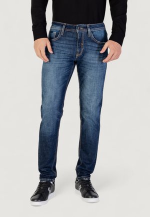 Dark blue denim jeans with a straight cut, prominent stitching, five-pocket design, and a fitted waistband. Worn with black sneakers.