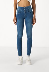 Jeans de mezclilla azul de cintura alta con cierre de cinco botones, dos bolsillos frontales y ajuste skinny, fabricados con material elástico similar al algodón.
