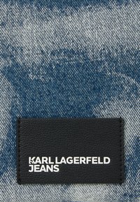 Kék és fehér gradienst mutató farmeranyag, fekete bőrrel ellátott folttal az alján, amelynek fehér, dombornyomott szövege: "KARL LAGERFELD JEANS".