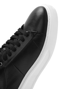 Sneaker in pelle nera con una tomaia liscia, pannelli laterali perforati e suola in gomma bianca. Punta arrotondati e design con lacci.