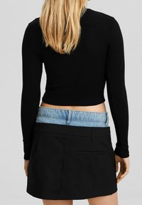 Top court à manches longues noir à côtes, associé à une ceinture de style denim et une jupe noire avec une poche arrière.