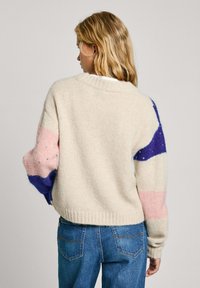 Pull en tricot crème avec une coupe oversize. Manches en blocs de couleur rose et bleu avec des accents texturés. Ourlet et poignets côtelés.