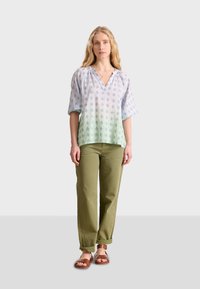 Blusa azul claro y blanca con un patrón, escote en V, mangas anchas y un degradado que se desvanece a verde, combinada con pantalones de color verde oliva.
