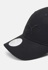 Cappellino da baseball nero realizzato in tessuto testurizzato. Presenta un logo ricamato sulla parte anteriore e un'etichetta circolare sulla visiera. Design con visiera curva.