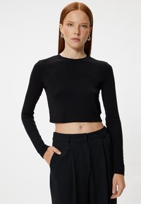 Zwarte lange mouw cropped top met een ronde halslijn, gemaakt van zachte stof, gecombineerd met hoge zwarte broeken. Eenvoudig ontwerp, zonder patronen.